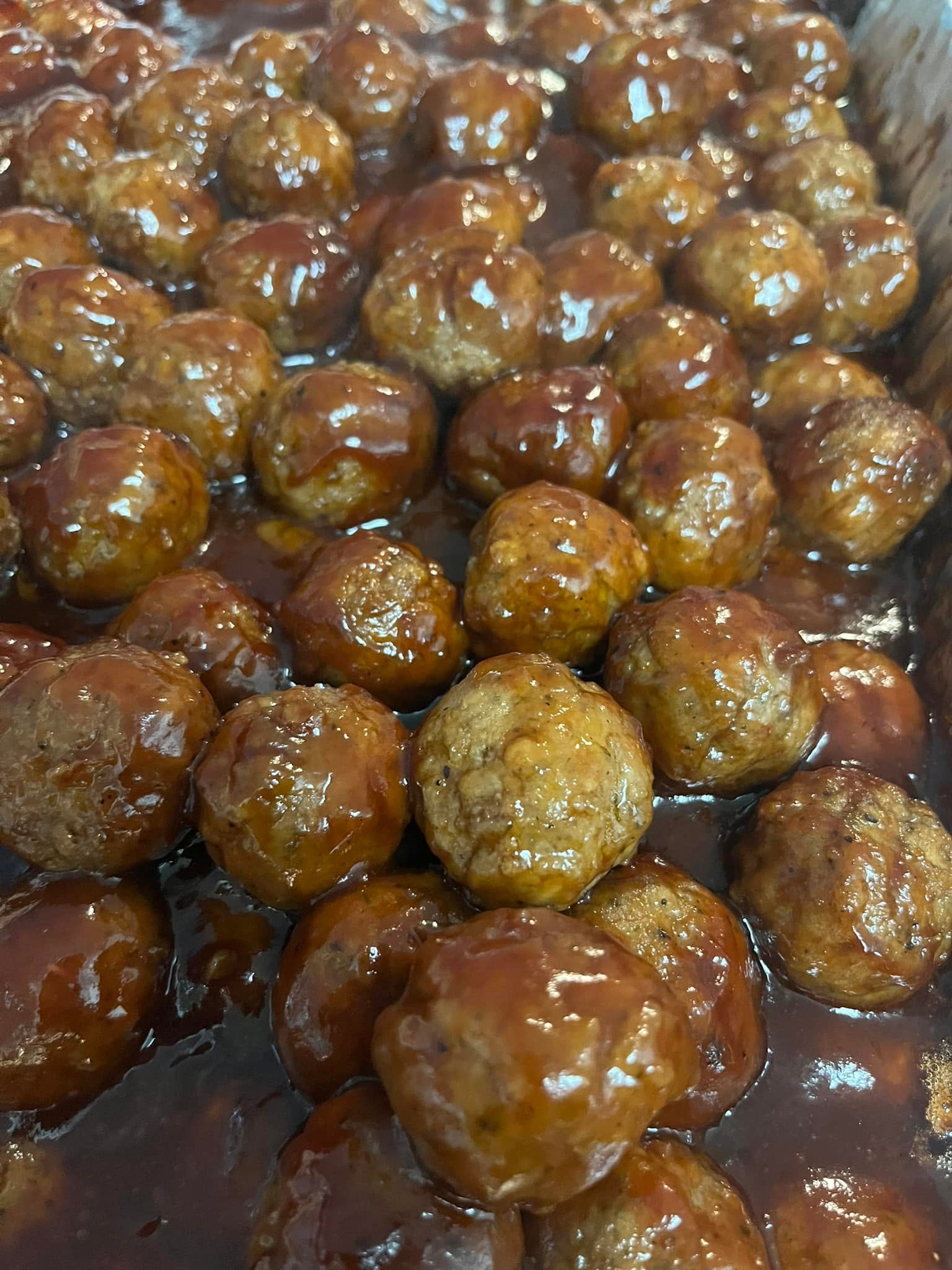Close-up of cooked meatballs covered in sauce, piled together on a surface.