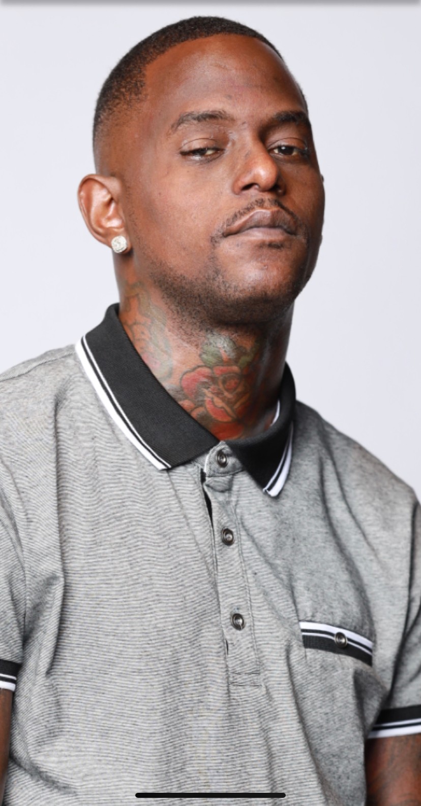 Young man with short hair and tattoos, wearing a gray polo shirt with black and white collar, looking serious.