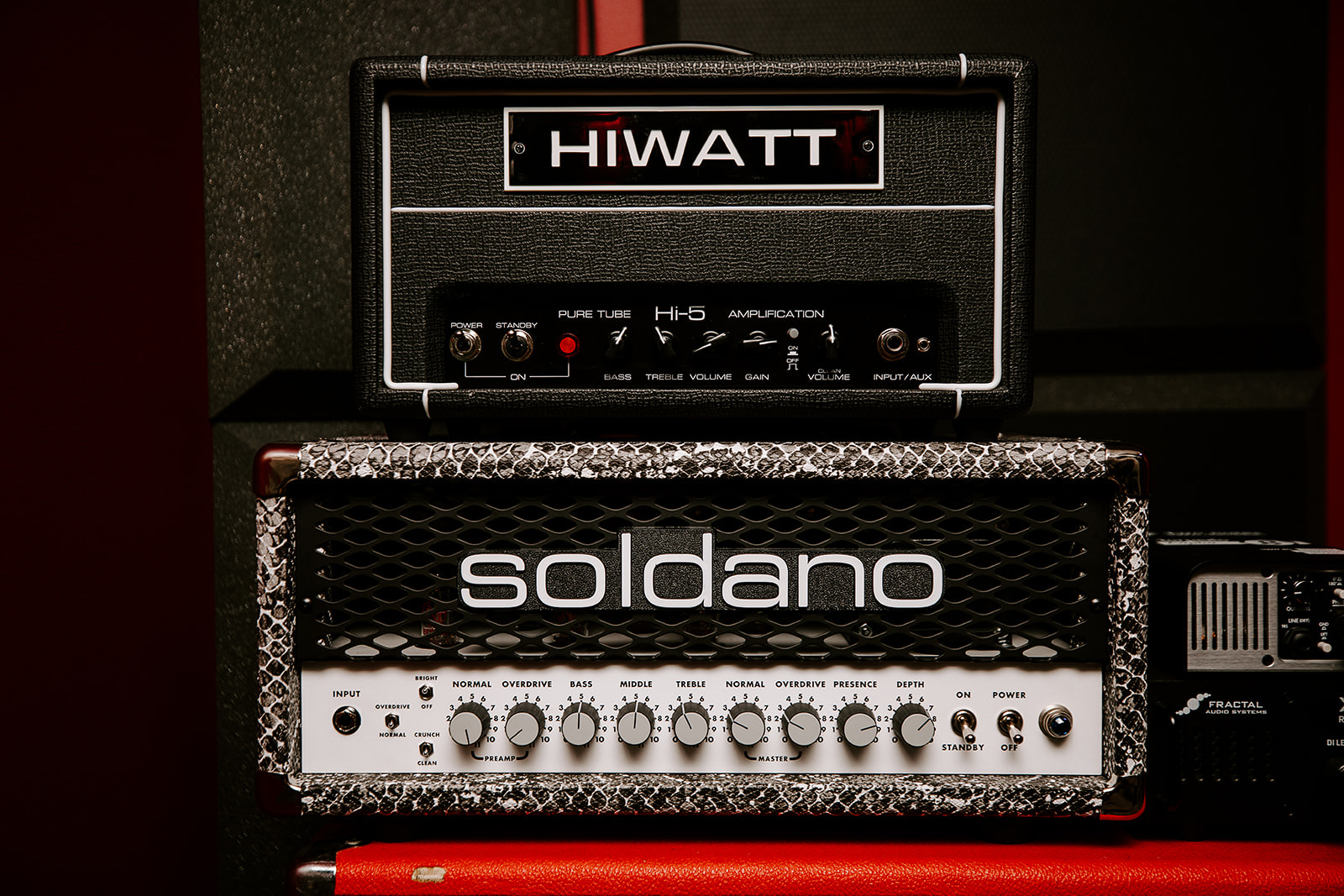 Guitar amplifier head on top of a speaker cabinet with a metal grille, brand names HIWATT and soldano visible, in a music setting.
