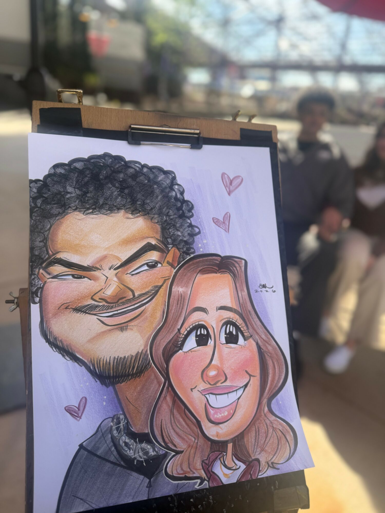 Caricature of a man and woman with exaggerated facial features, smiling, with pink hearts around them.
