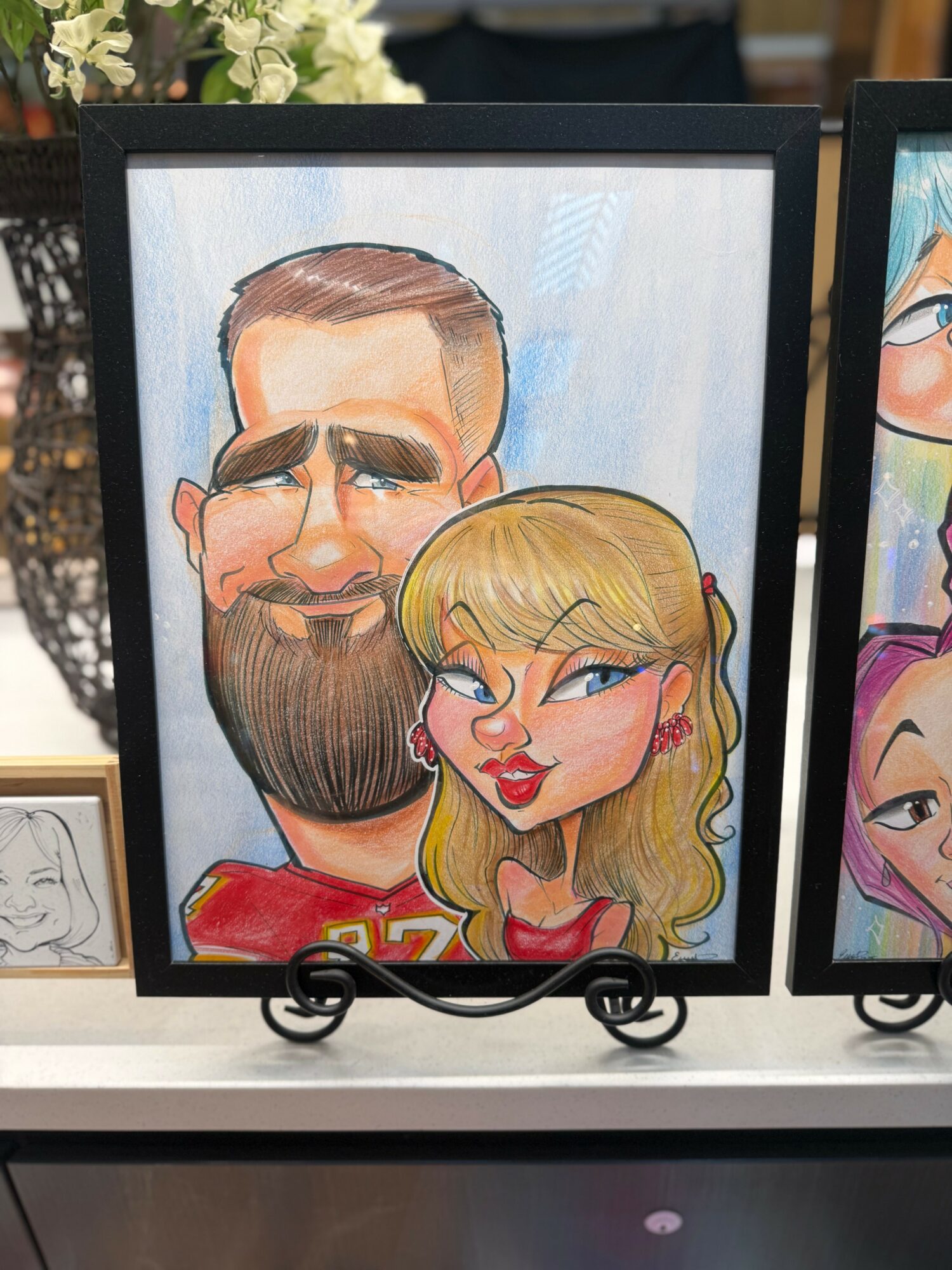 Caricature of a man with a beard and a woman with blonde hair, both smiling, in a black frame.