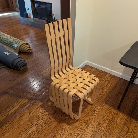 Wooden chair with slatted back and seat, placed on hardwood floor next to a wall and table.