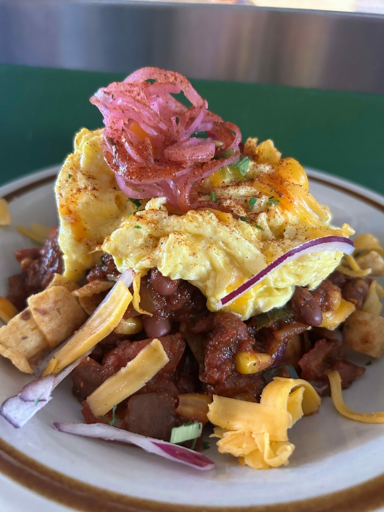 Plate with scrambled eggs, beef, corn, shredded cheese, and pickled onions, viewed sideways.