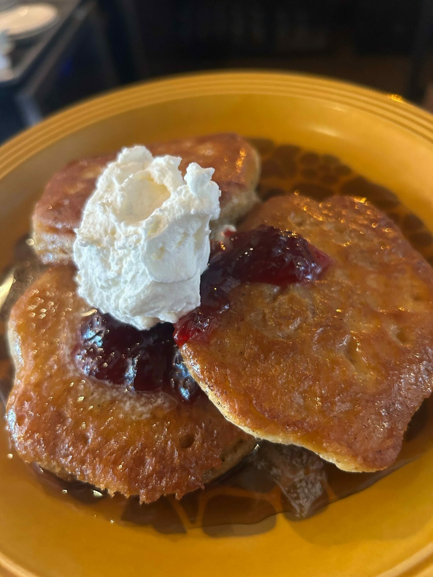 Three French toast slices with syrup and a dollop of whipped cream on a yellow plate.