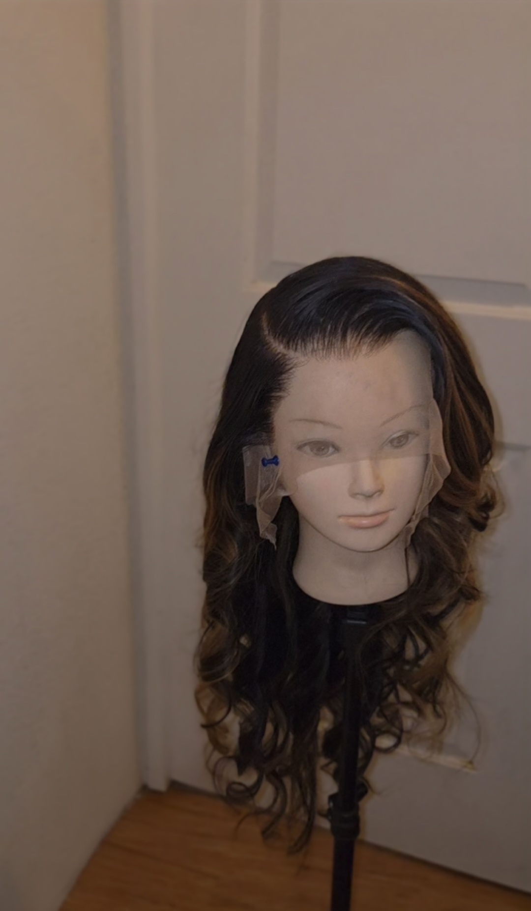 A mannequin head with long, wavy brown hair on a stand in front of a door.