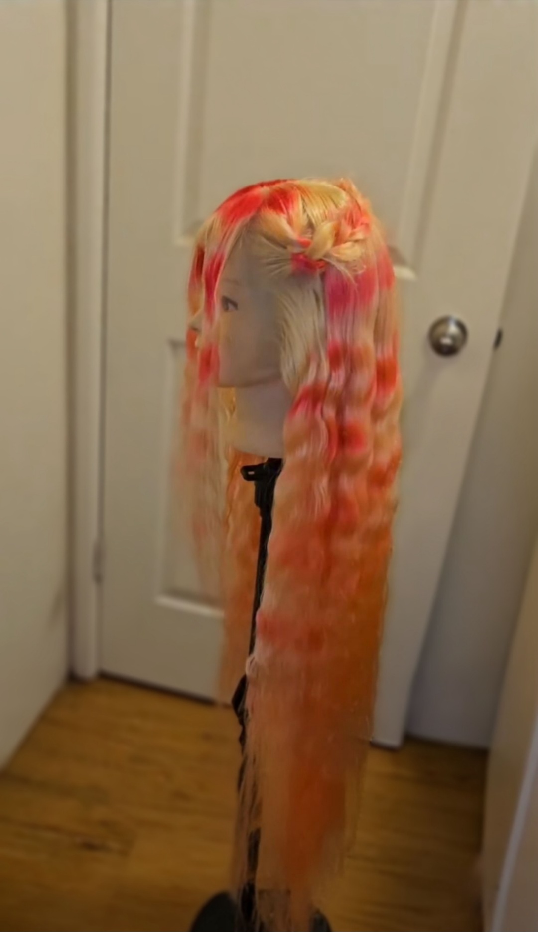 Person with long, curly, multicolored hair standing in front of a door, facing away, with a white face mask.