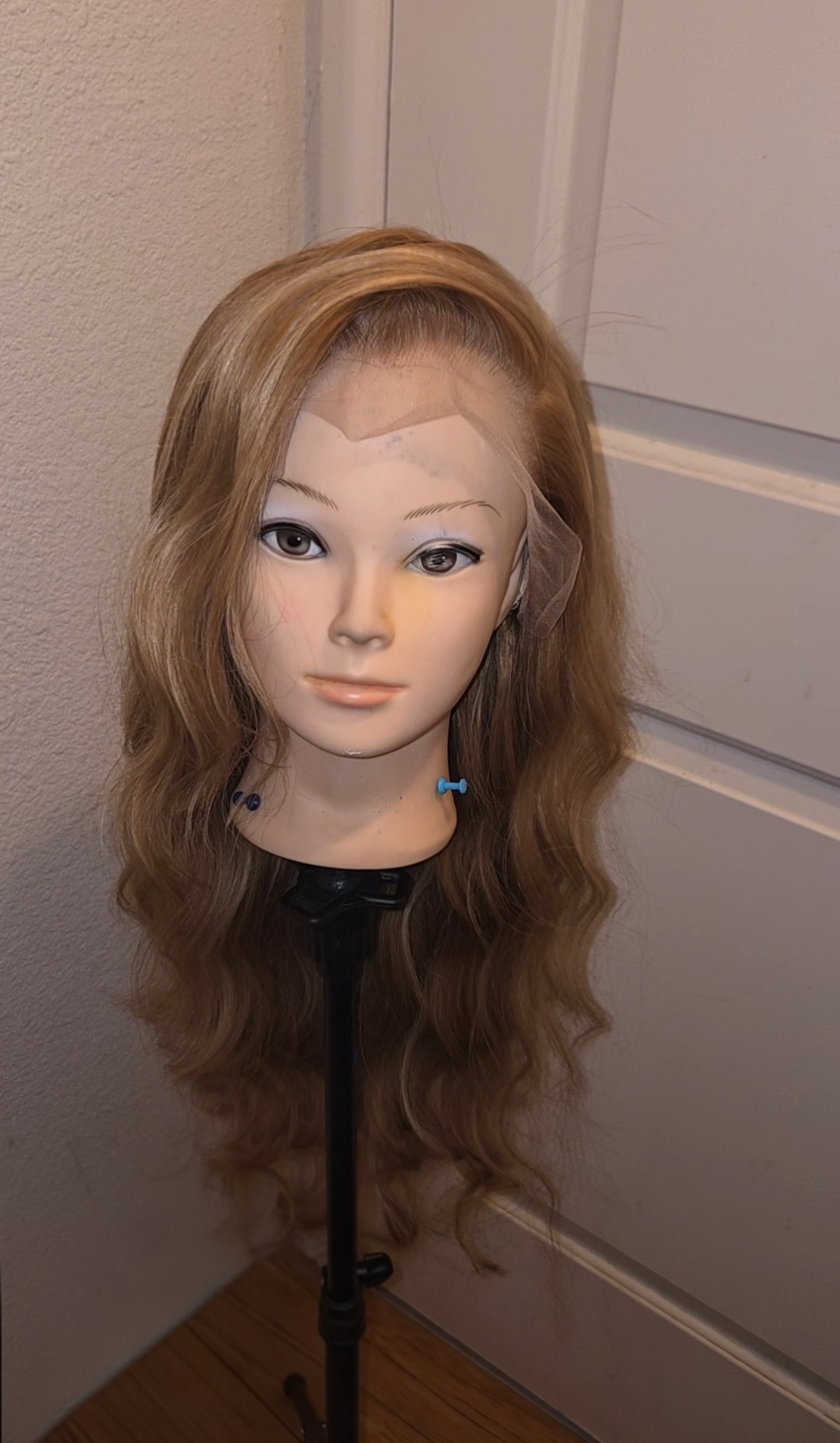 Mannequin head with long, wavy light brown hair and makeup, on a stand in front of a door.
