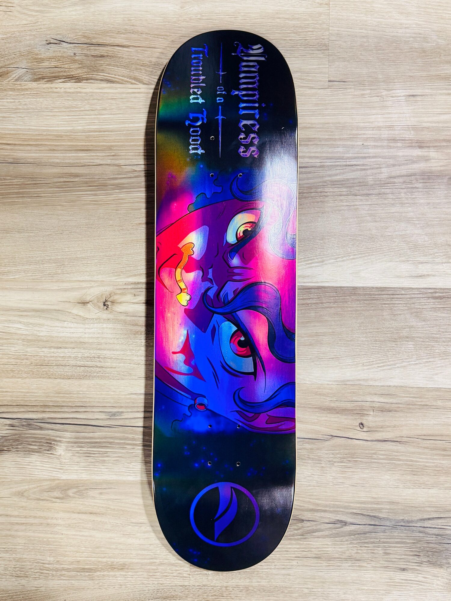 Skateboard deck with colorful unicorn and moon design, text, and logo on a wooden surface.