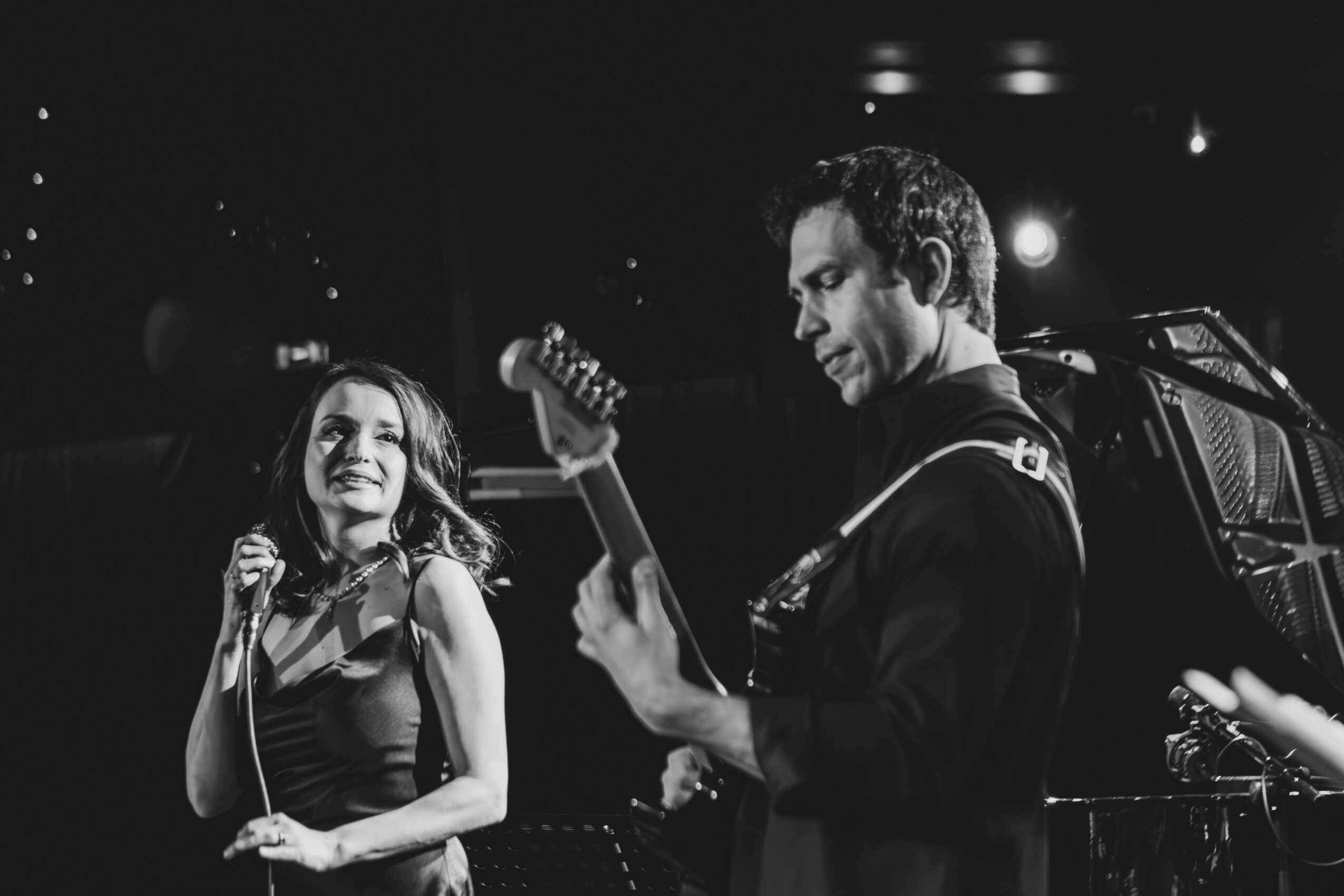 A woman singing into a microphone and a man playing guitar on stage in black and white.