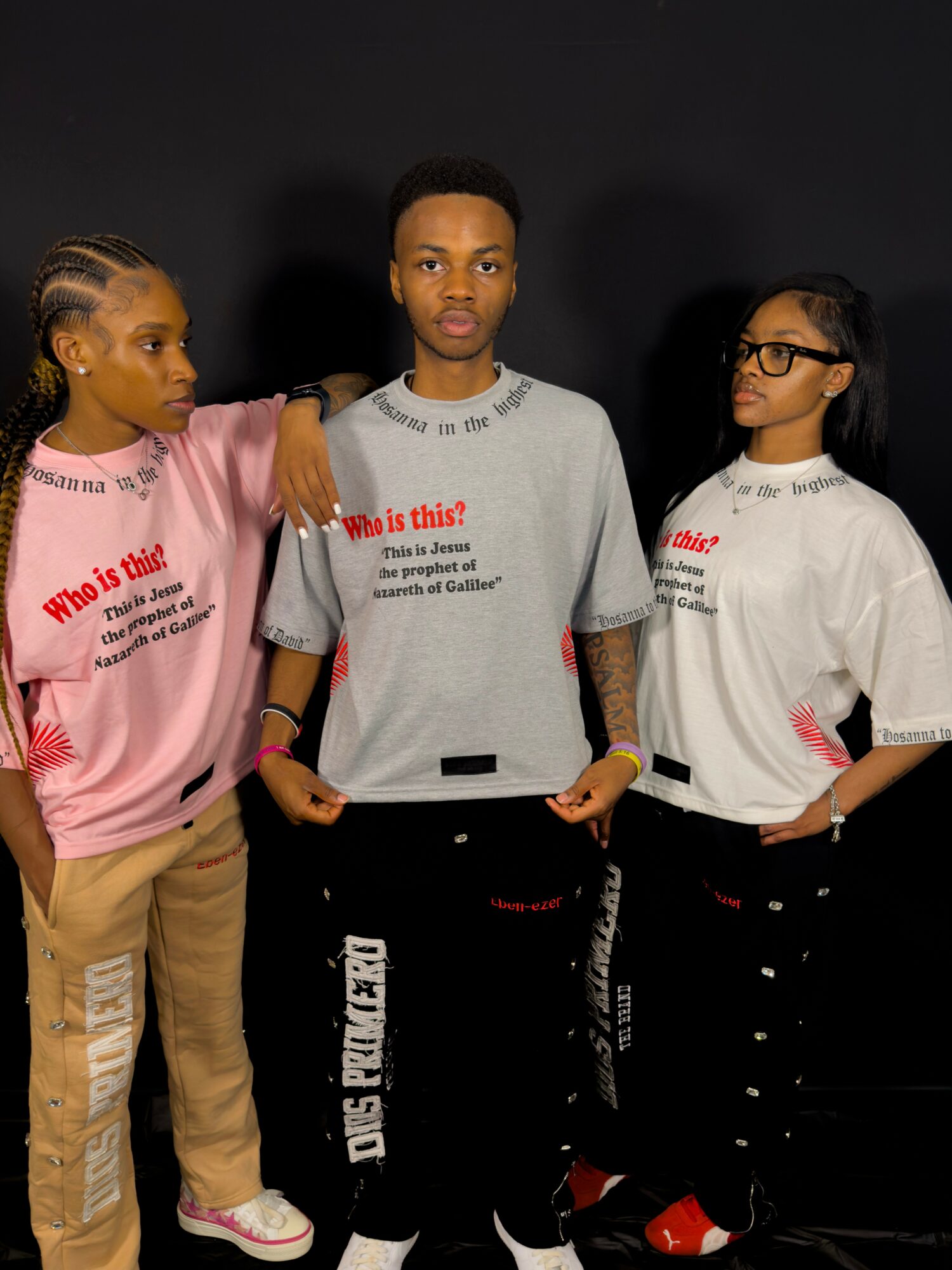 Three young people standing against a dark background, wearing casual clothing and looking in different directions.