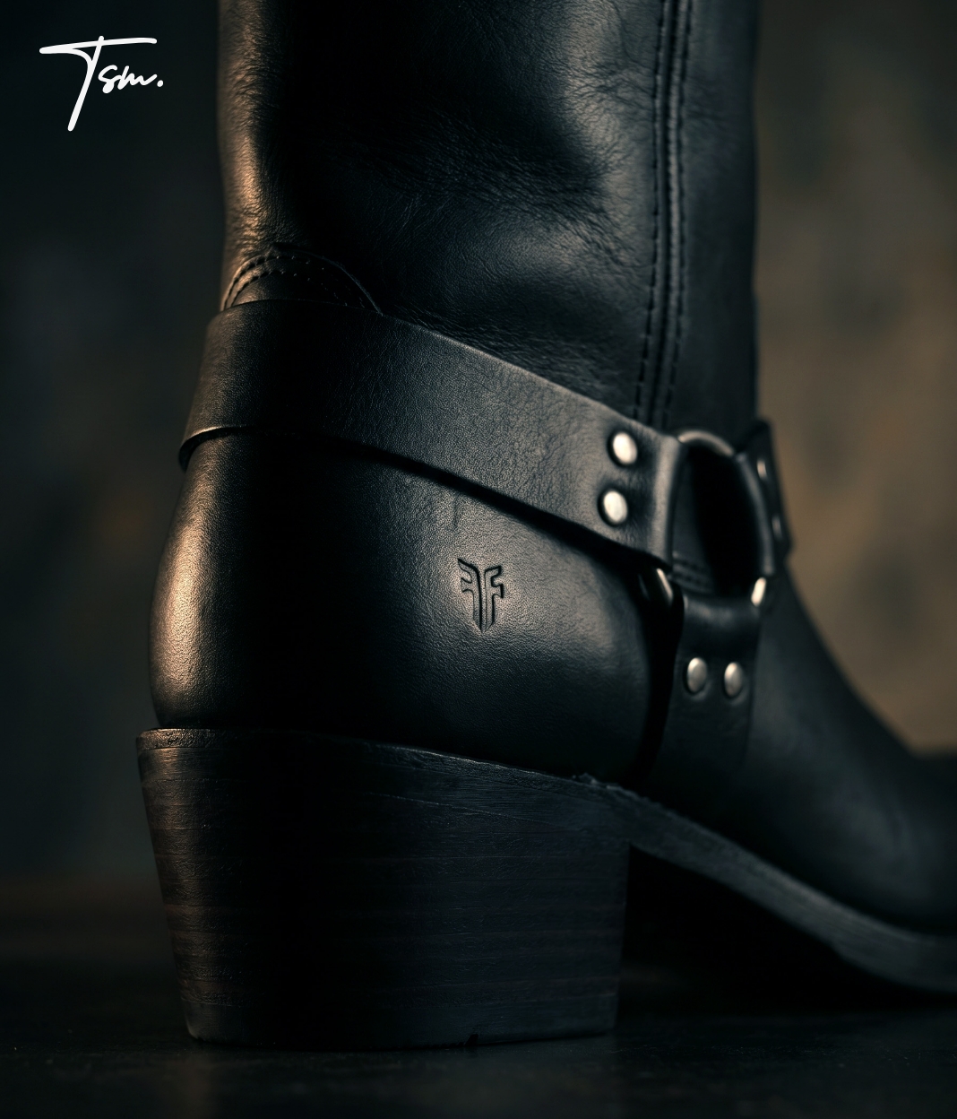 Close-up of a black leather boot with a strap and metal buckle, showing the heel and side details.