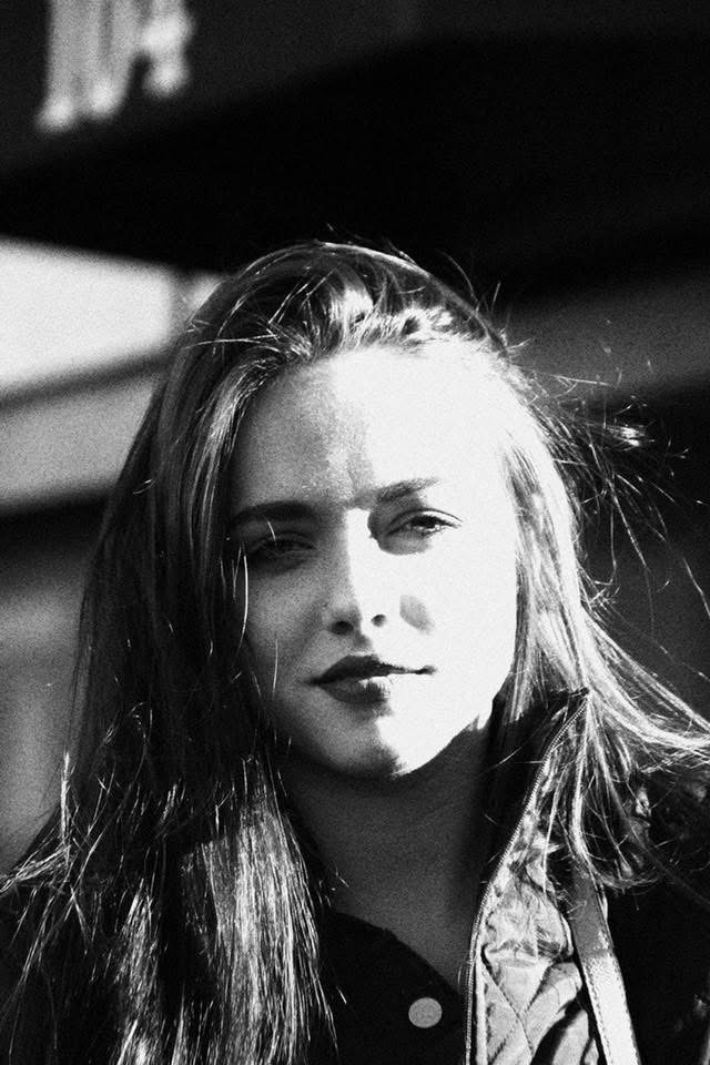 Black and white portrait of a young woman with long hair, looking at the camera with sunlight on her face.