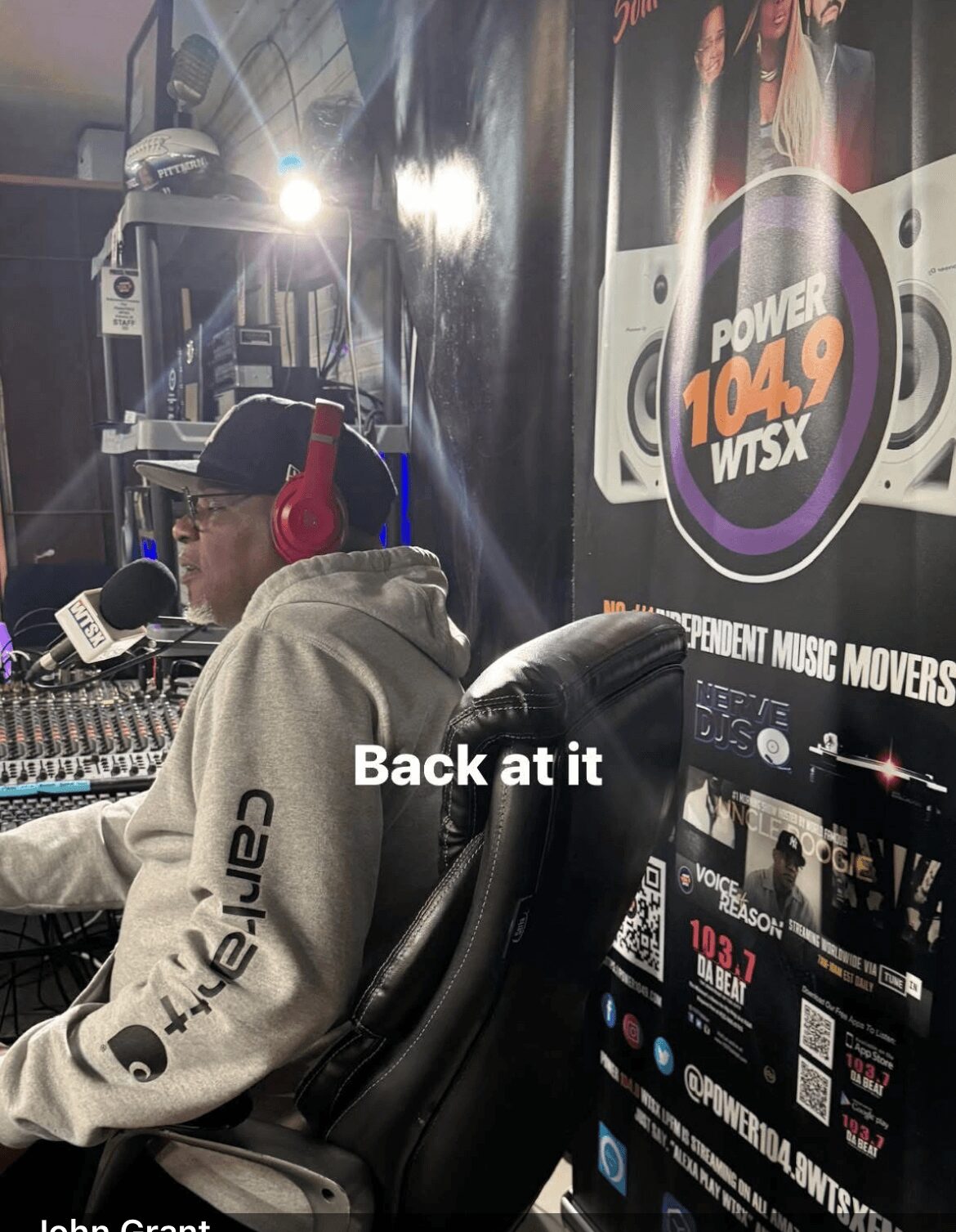 Person wearing a gray hoodie and red headphones sitting at a radio station with equipment and a Power 104.9 WTSX poster behind them.