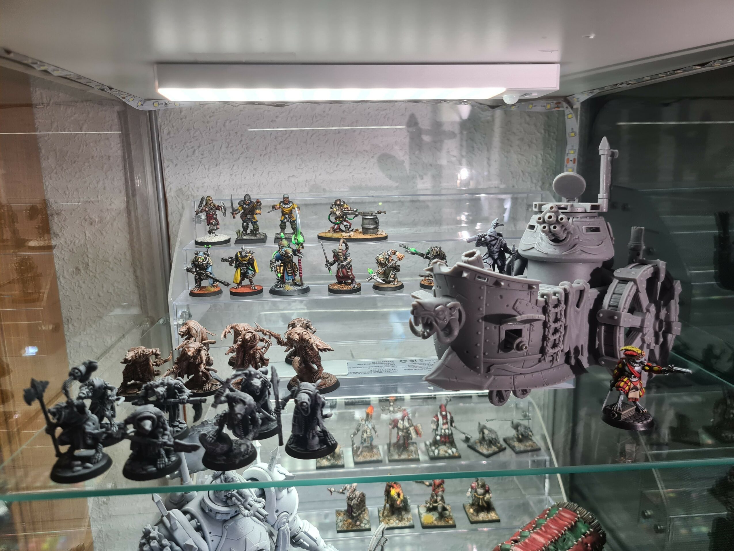 Display case with miniature figures and a large tank model, arranged on glass shelves inside a glass cabinet.
