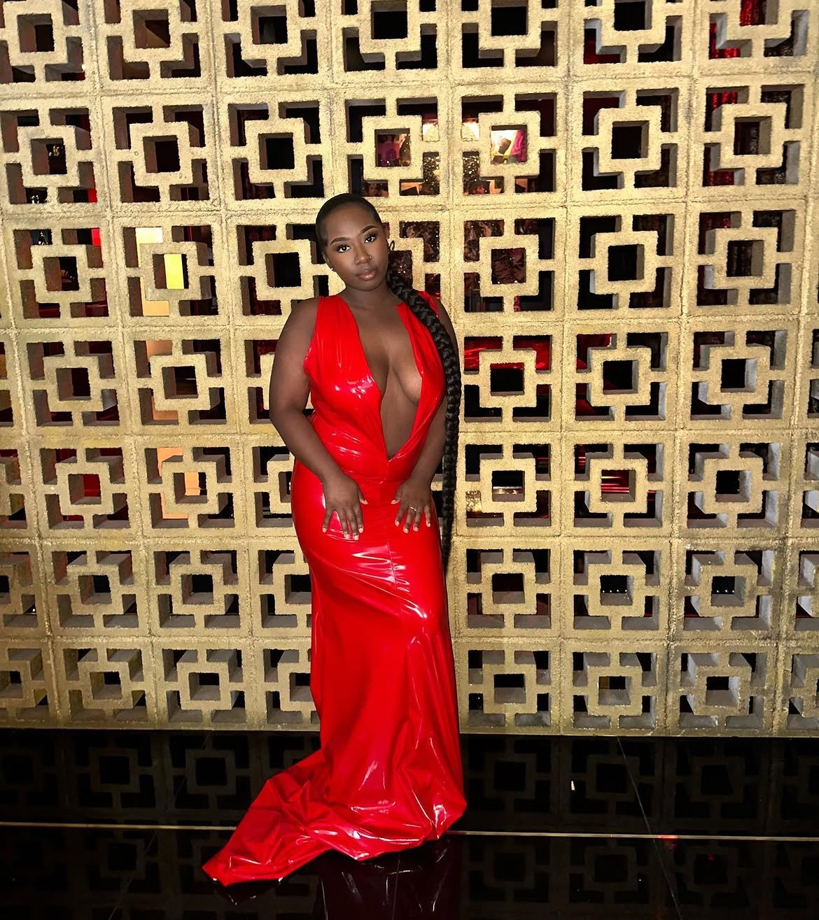 Woman in a red dress standing in front of a decorative wall with geometric patterns.