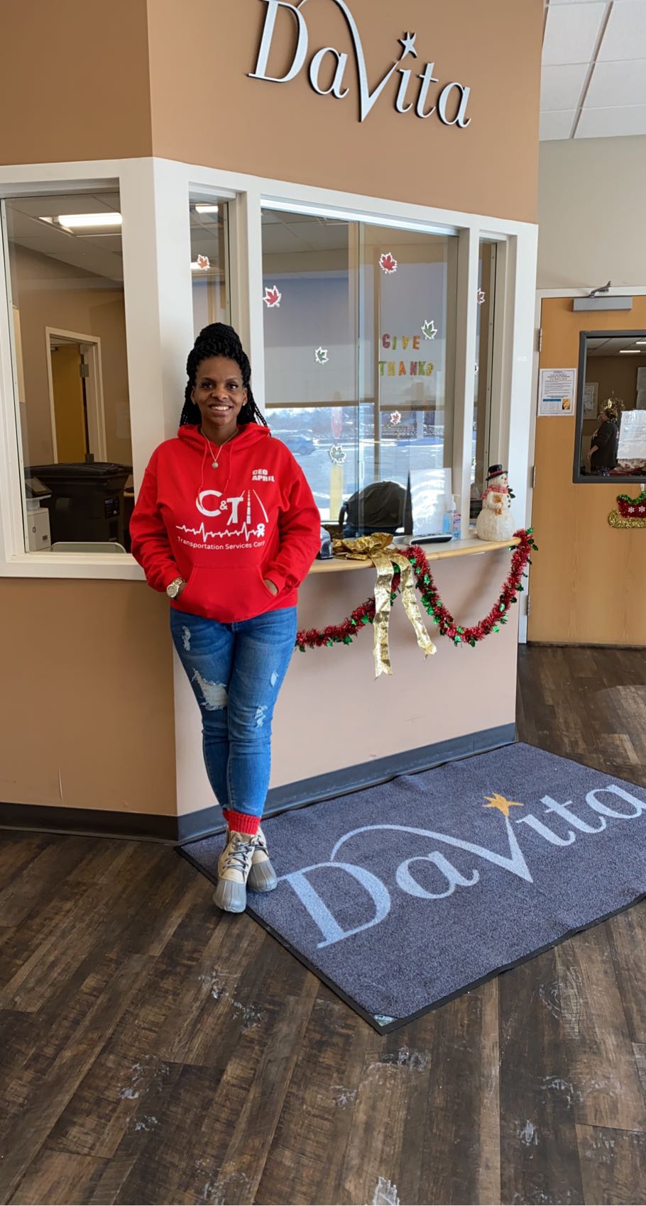 Woman standing in front of a window with holiday decorations, wearing a red hoodie and jeans, inside a store named DaVita.