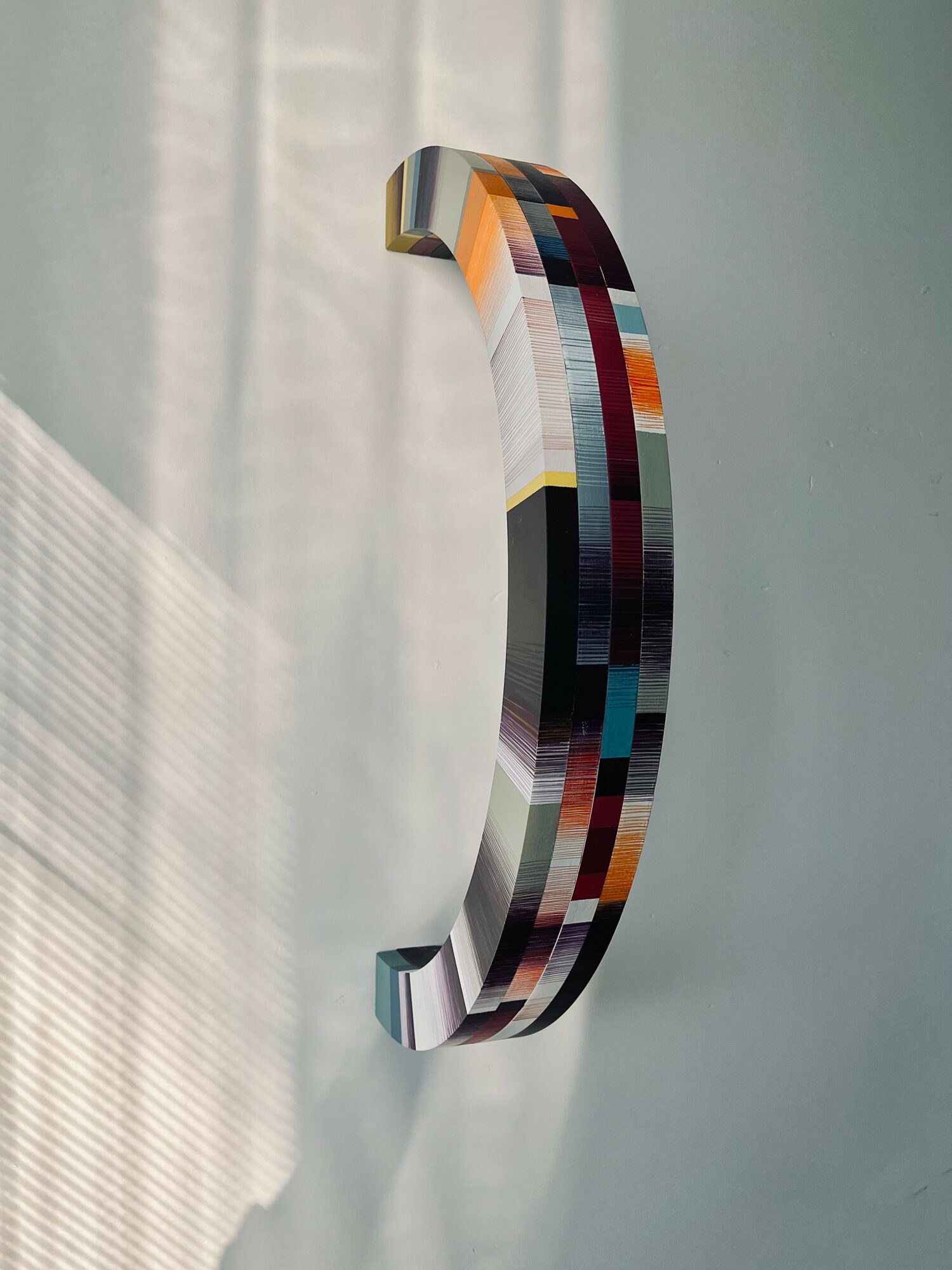 Colorful pixelated sculpture mounted on a wall, with a curved shape and a mix of various colors.