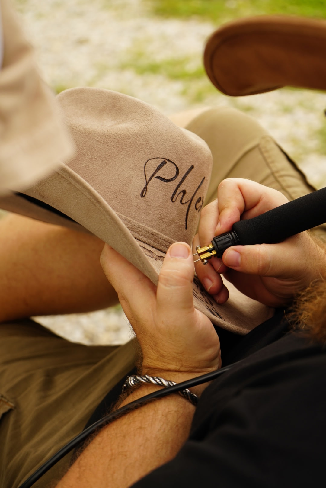 Person signing a beige hat with a black marker outdoors, with grass in the background.