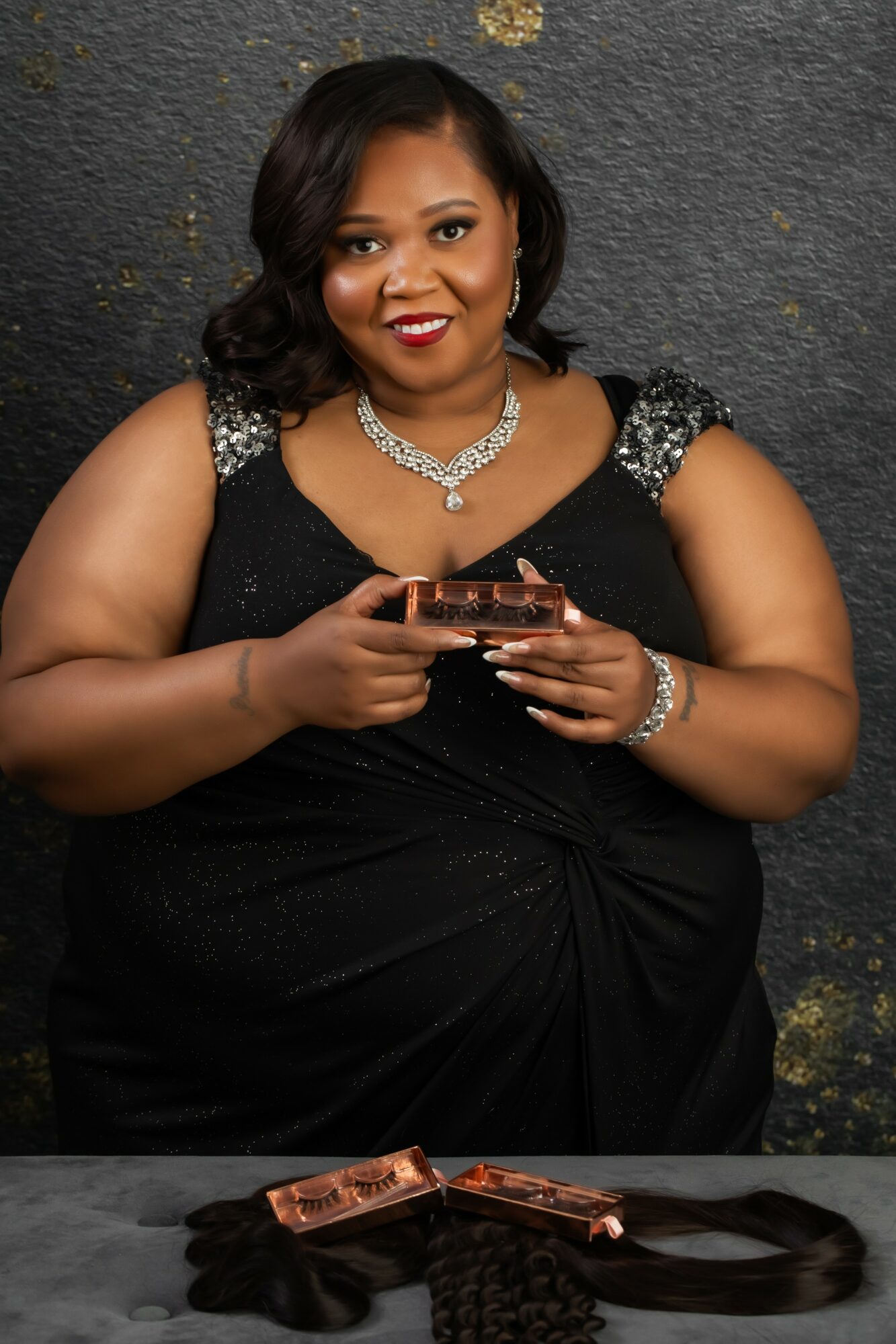 Woman in black dress holding a phone, smiling, against dark textured background.
