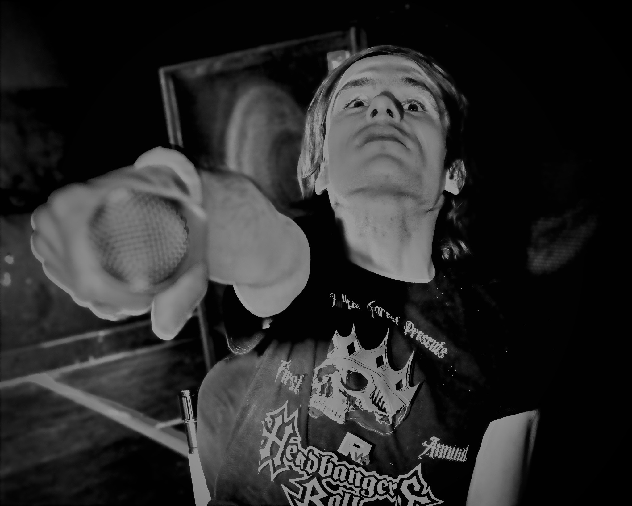 Person with short hair pointing directly at the camera, wearing a graphic T-shirt, in a dark environment.