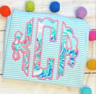 Fabric with embroidered monogram surrounded by colorful pom-poms, on a striped background.