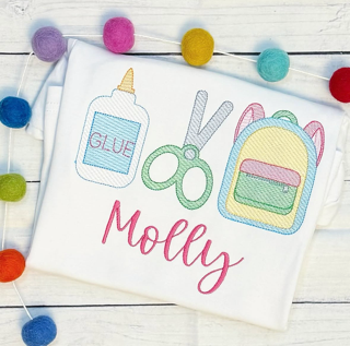 White cloth with colorful craft-themed embroidery, including glue, scissors, and a backpack, with the name Molly, surrounded by pom-poms.