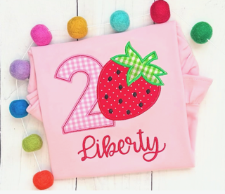 Pink cloth with a strawberry, the number 2, and the word Liberty, surrounded by colorful pom-poms.