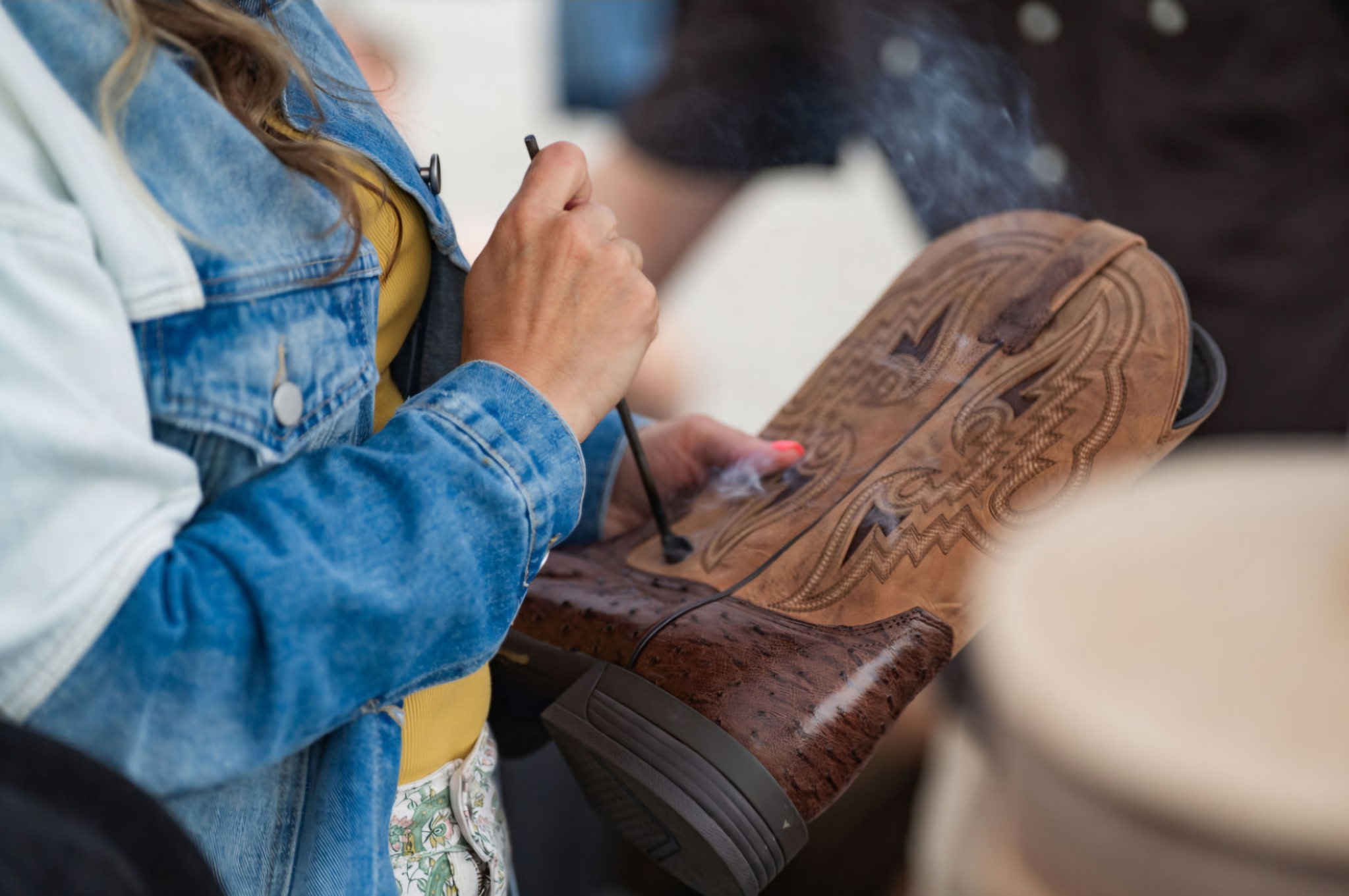 Person holding a pen and drawing on a wooden object, with another person nearby. Focus on hands and object.