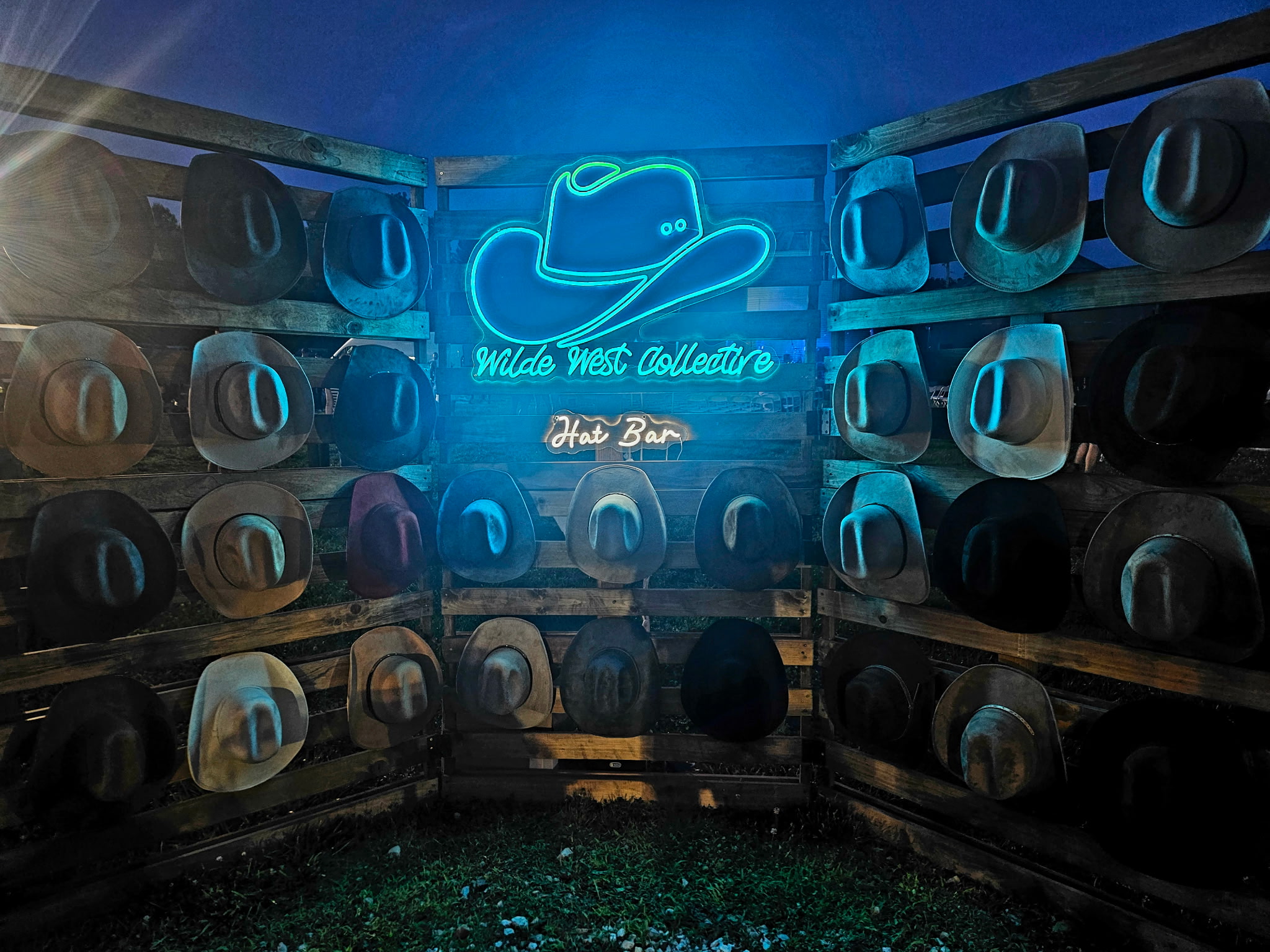 Neon sign with a hat and text, surrounded by stacked speakers in a dark room.