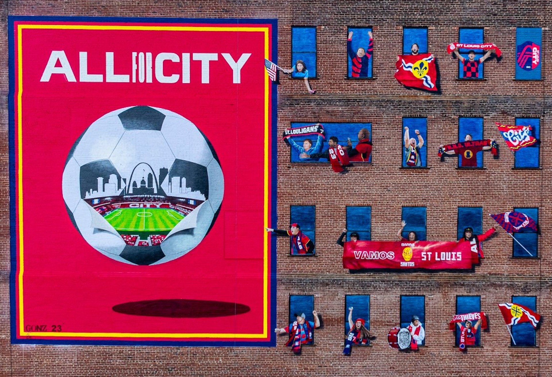Large colorful banner with a soccer ball and city skyline, surrounded by small decorated boxes on a brick wall.