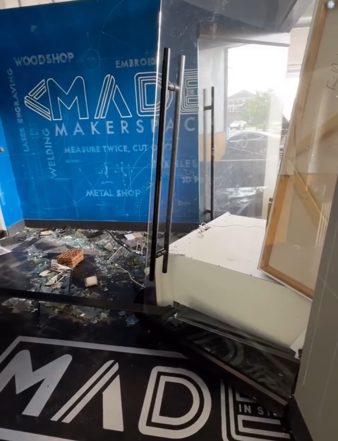 Interior view showing a glass door, a window, and construction debris on the floor, with a blue sign in the background.
