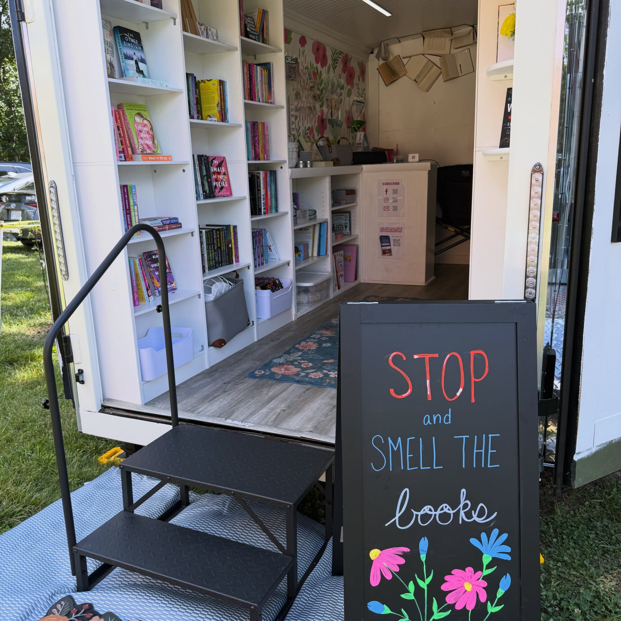 Bookshelf inside a small shop with a chalkboard sign reading 'STOP and SMELL THE books'.