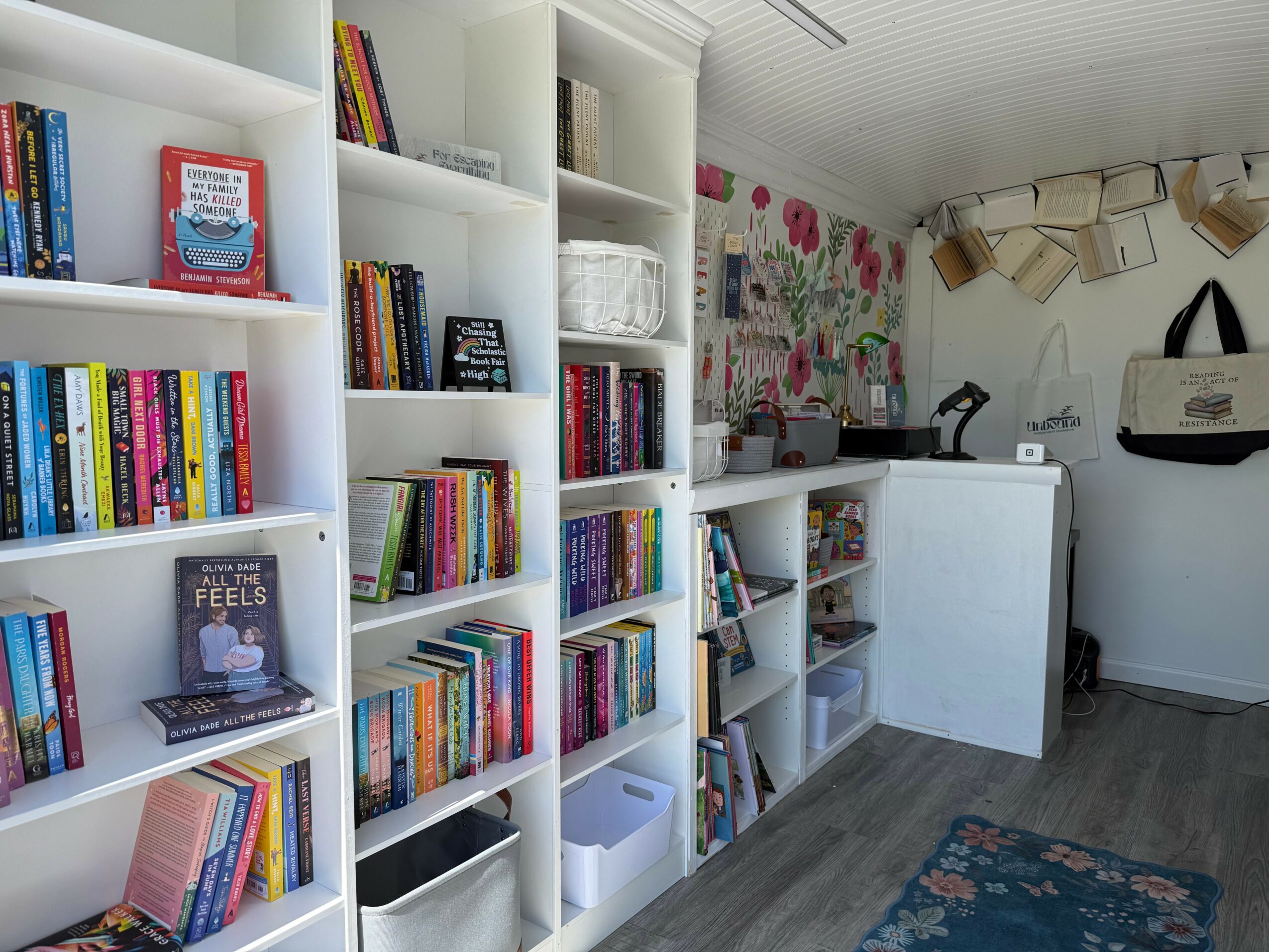 Bookshelves filled with books and decorative items in a room with a floral wall and a white counter.