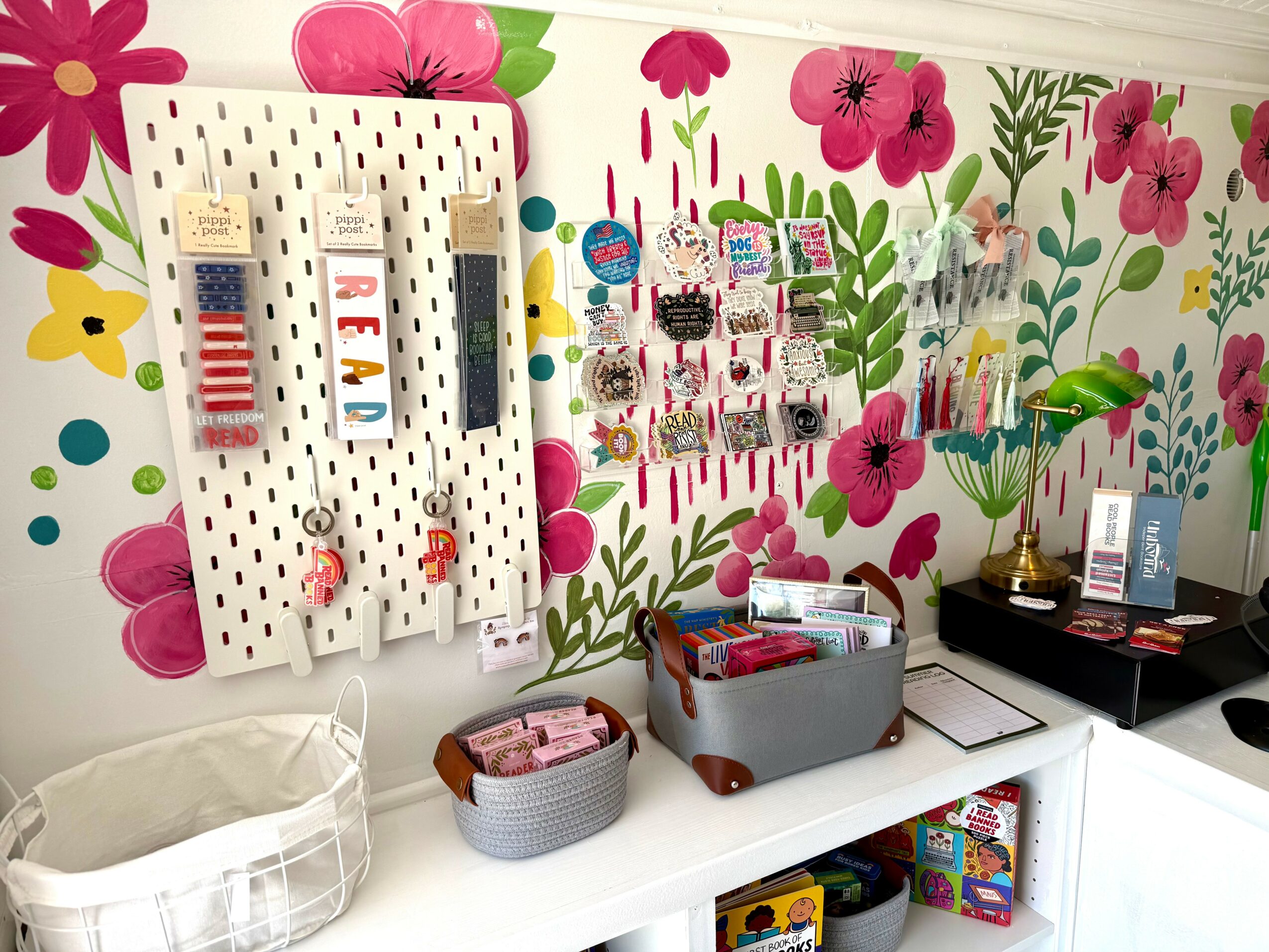 Display wall with colorful floral mural, organized craft supplies, and a white table with storage baskets and a plant.