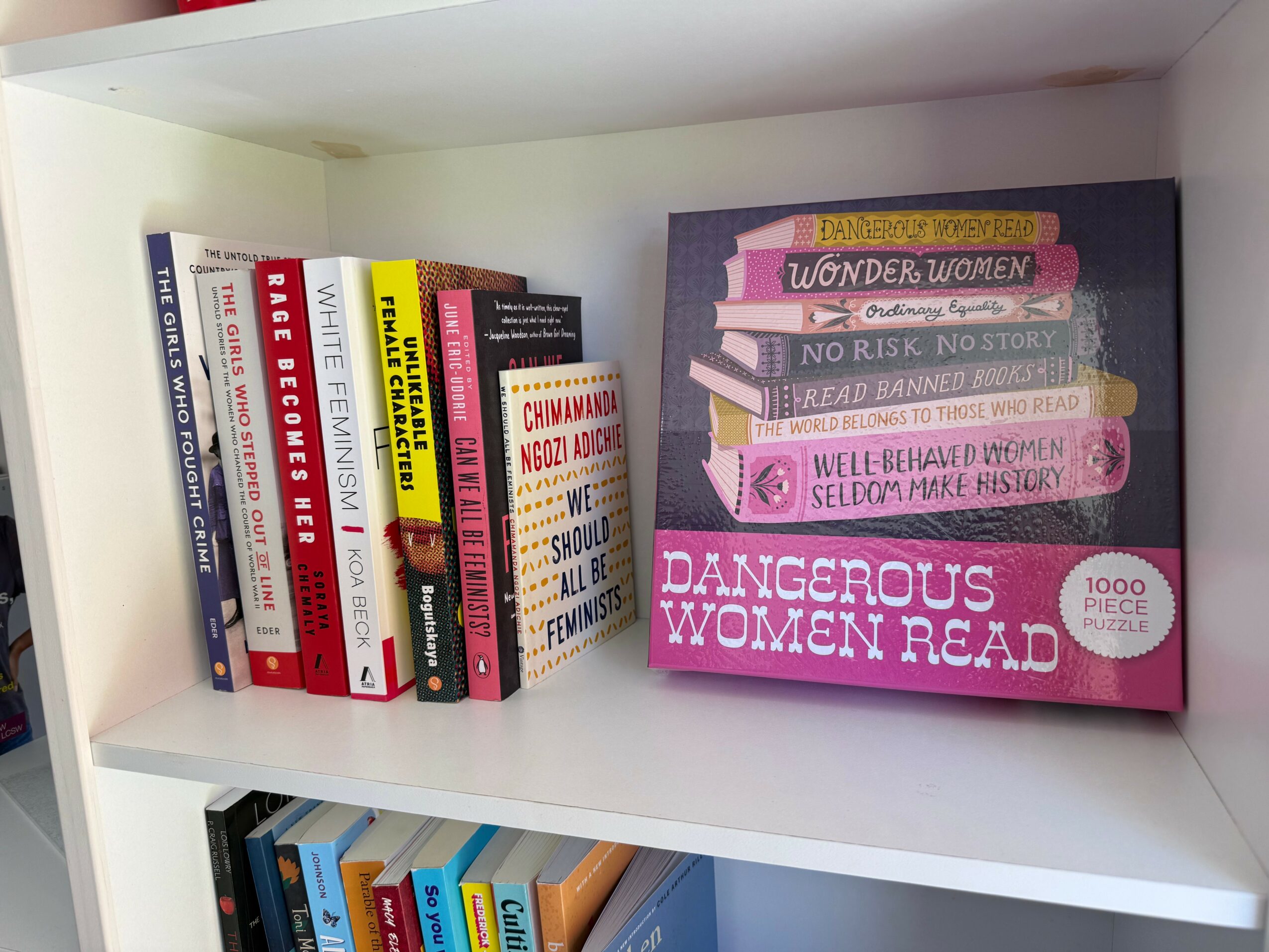 Books on a white shelf, including titles about women, danger, and stories, with a pink box labeled 'Dangerous Women Read'.