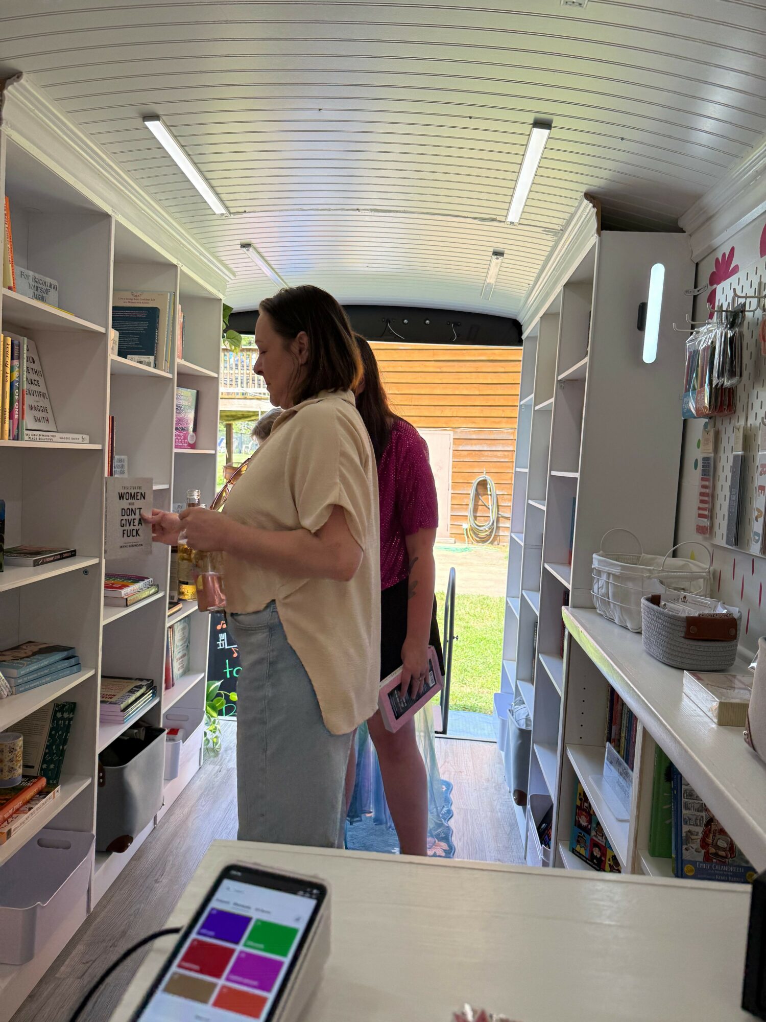 Woman browsing books in a bookstore with shelves and a bright window in the background.