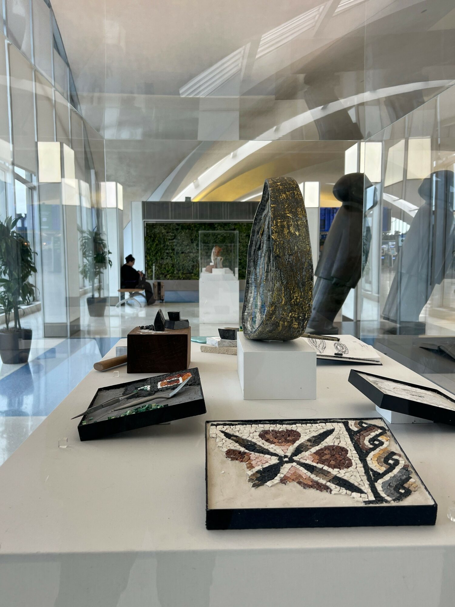 Display of decorative objects and artwork on a white table in a modern, glass-walled space with natural light.