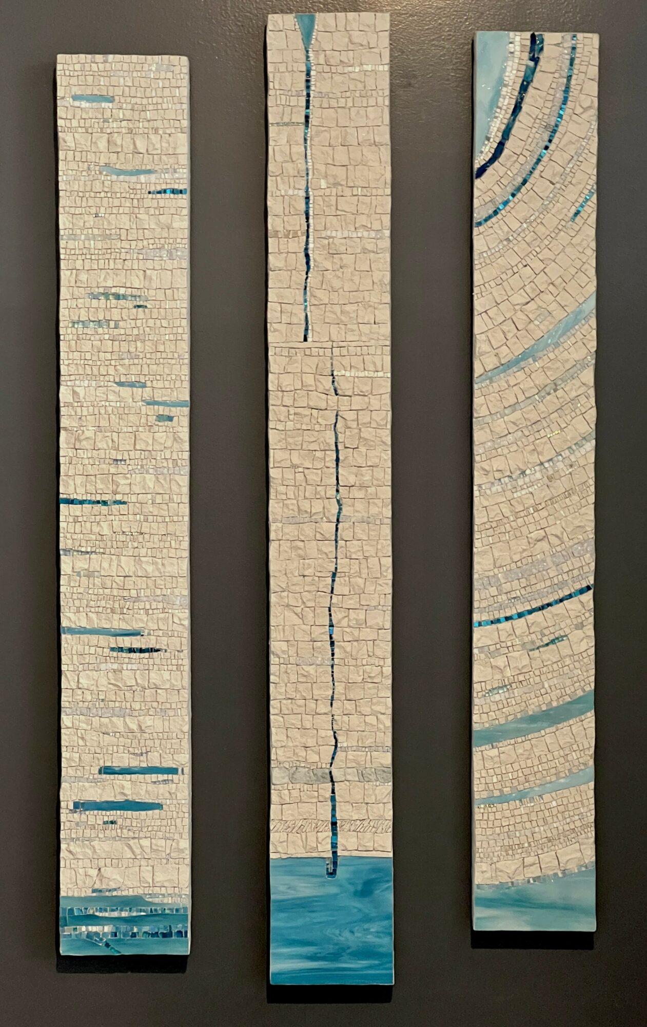 Three vertical wooden panels with painted blue and beige patterns, one cracked in the middle, on a neutral background.