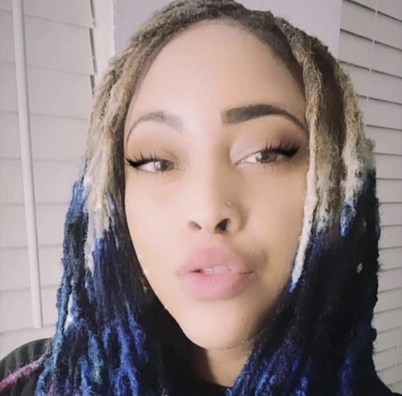 Close-up of a woman with styled dreadlocks, looking at the camera with a neutral expression.