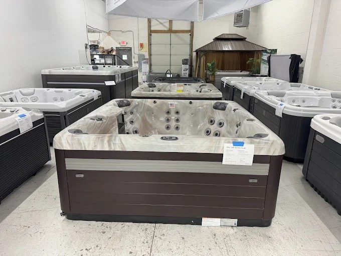 A showroom with multiple hot tubs and spas displayed, with a wooden structure and appliances in the background.