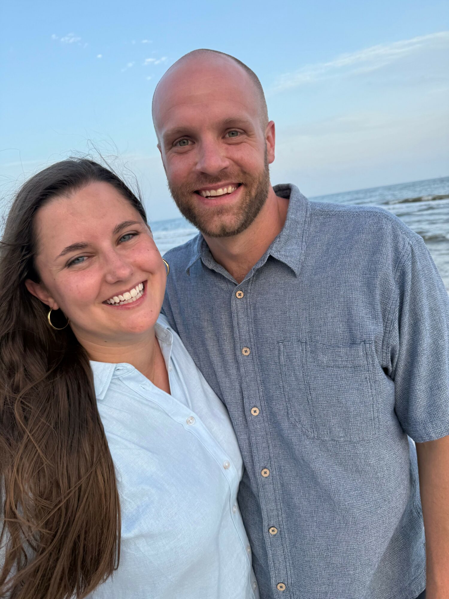 Two smiling people, a man and a woman, outdoors with a blue sky background.