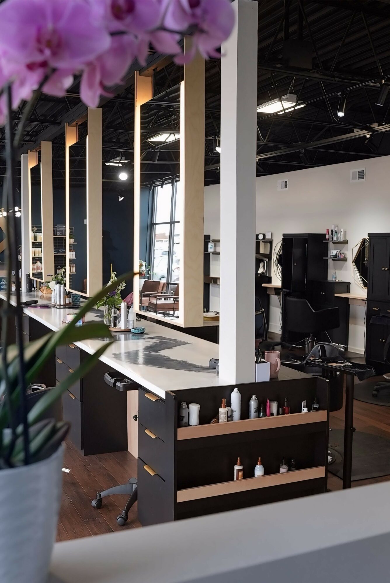 Interior of a modern salon with chairs, mirrors, and hair styling stations, seen through a foreground of pink flowers.
