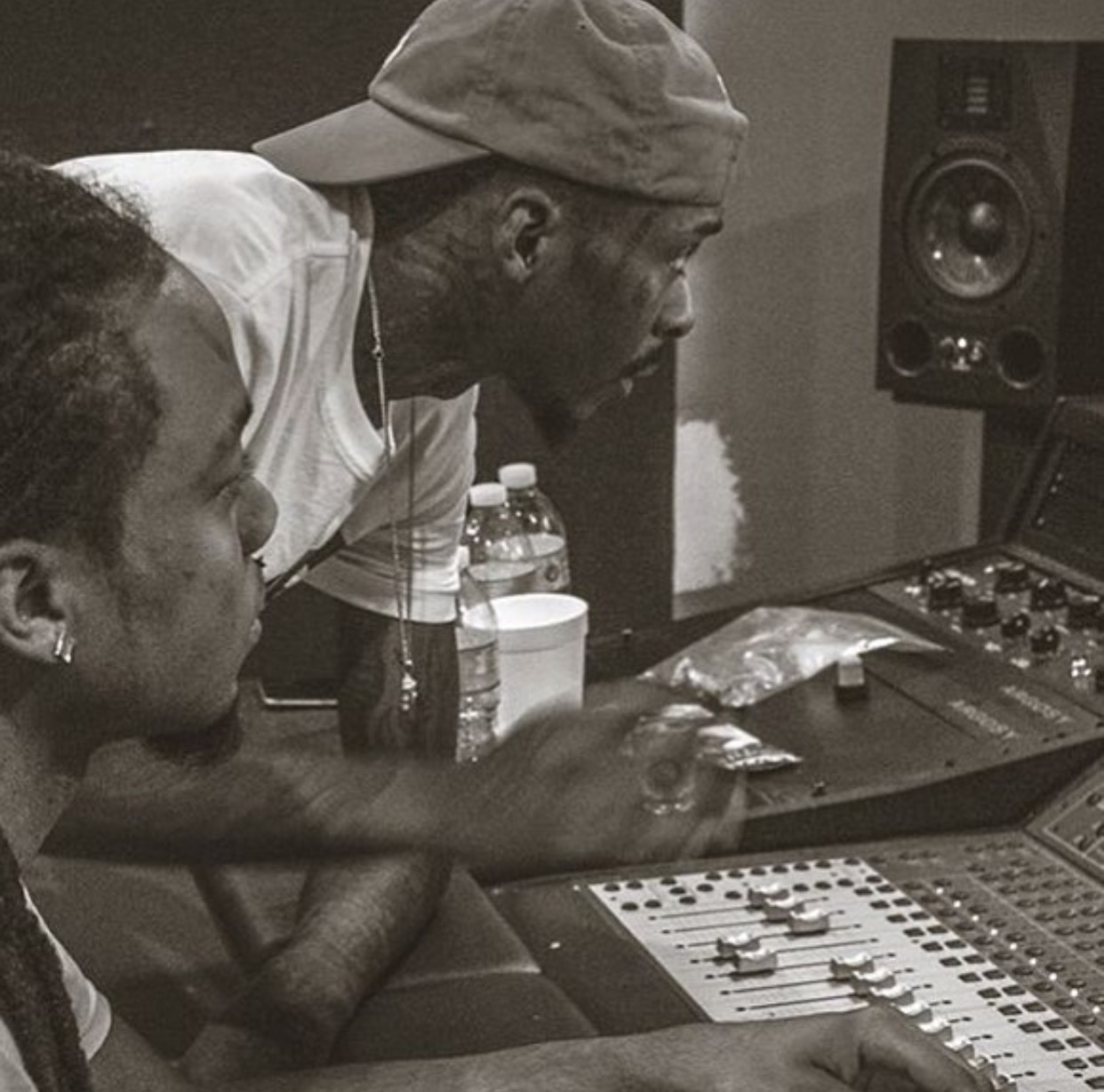 Two people in a recording studio, one adjusting sound equipment, with a speaker in the background.