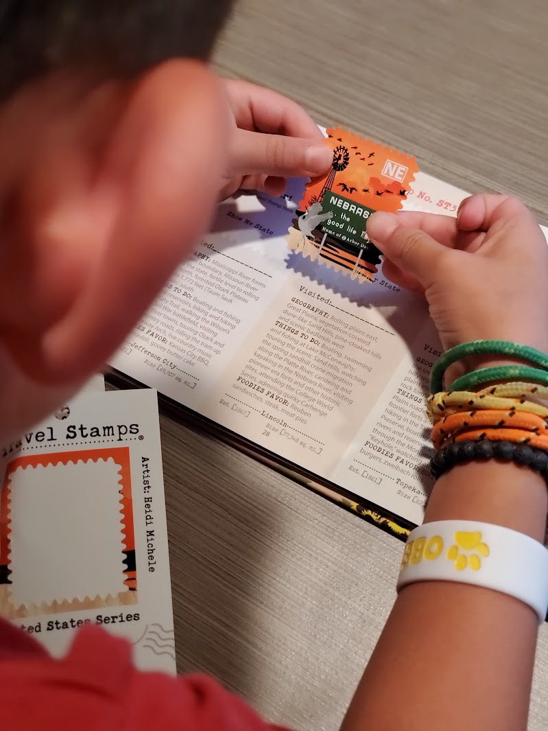 Person holds colorful tickets over open book, with travel stamps and wristbands visible, on a wooden surface.