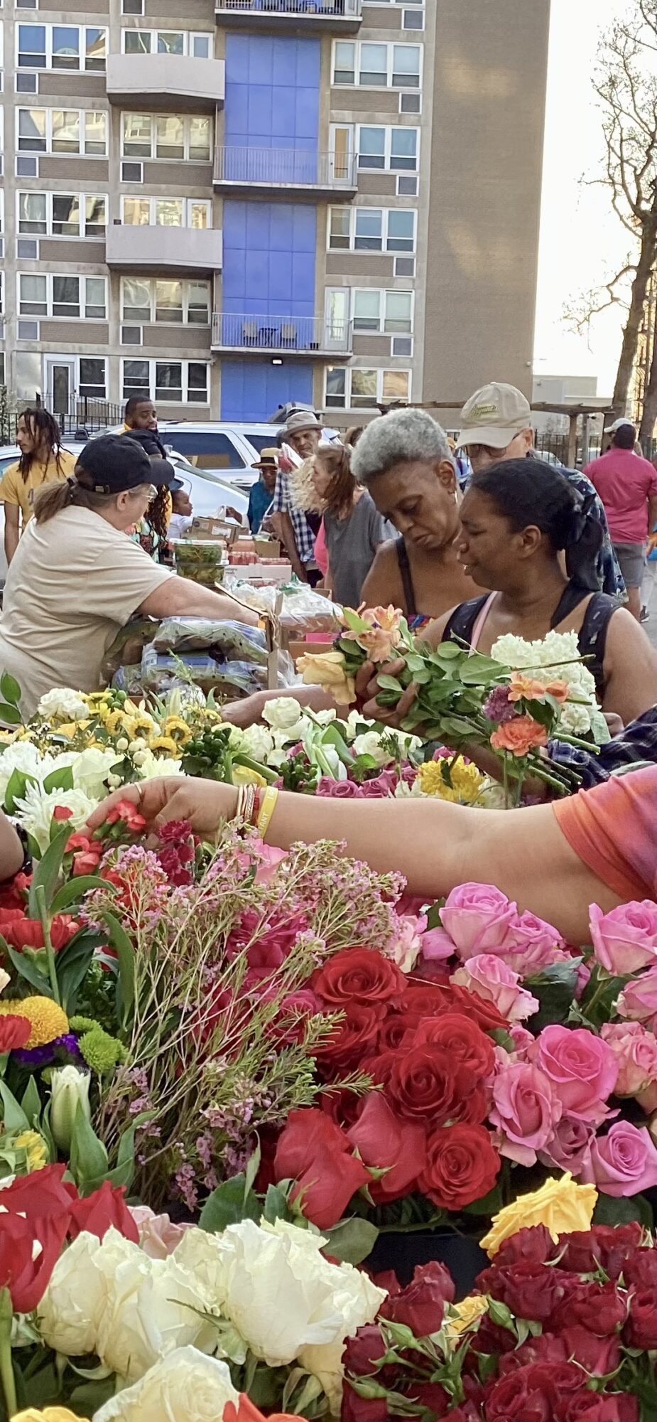 People shopping at an outdoor flower market with colorful flowers and a building in the background.