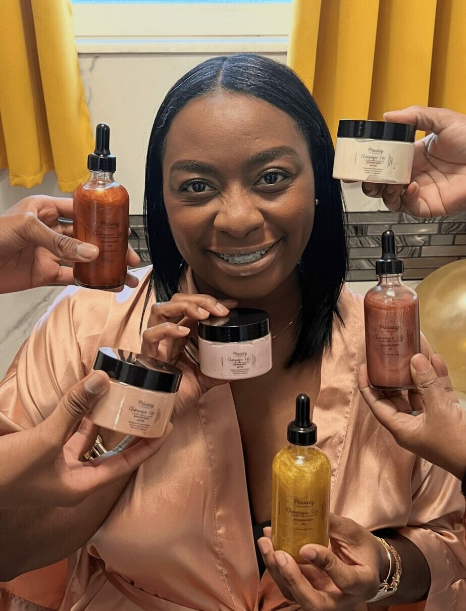 Smiling woman holding skincare products in a room with yellow curtains, surrounded by bottles and jars, looking at the camera.