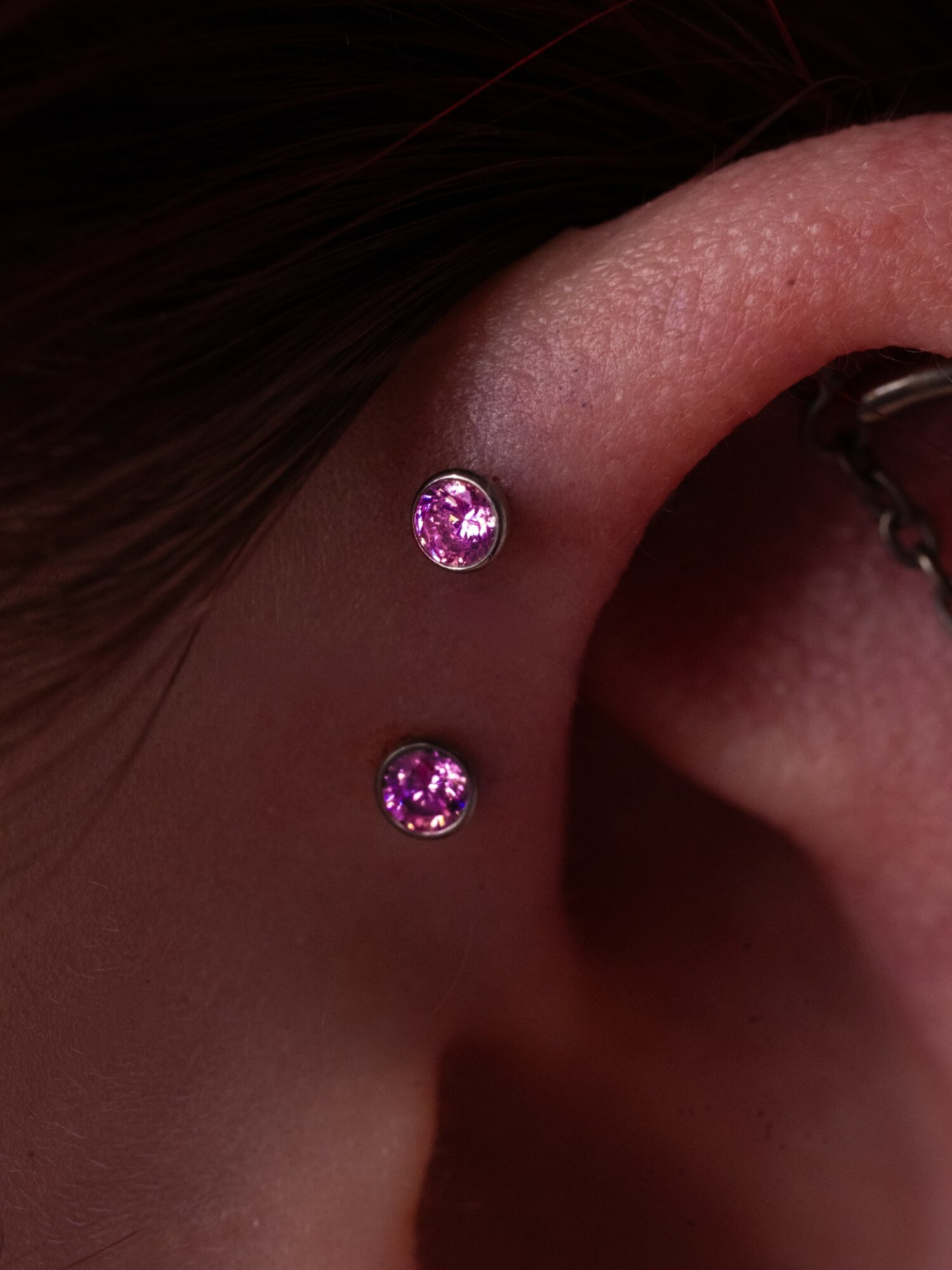 Close-up of a person's ear with two purple gemstone earrings, one above the other, on the earlobe.