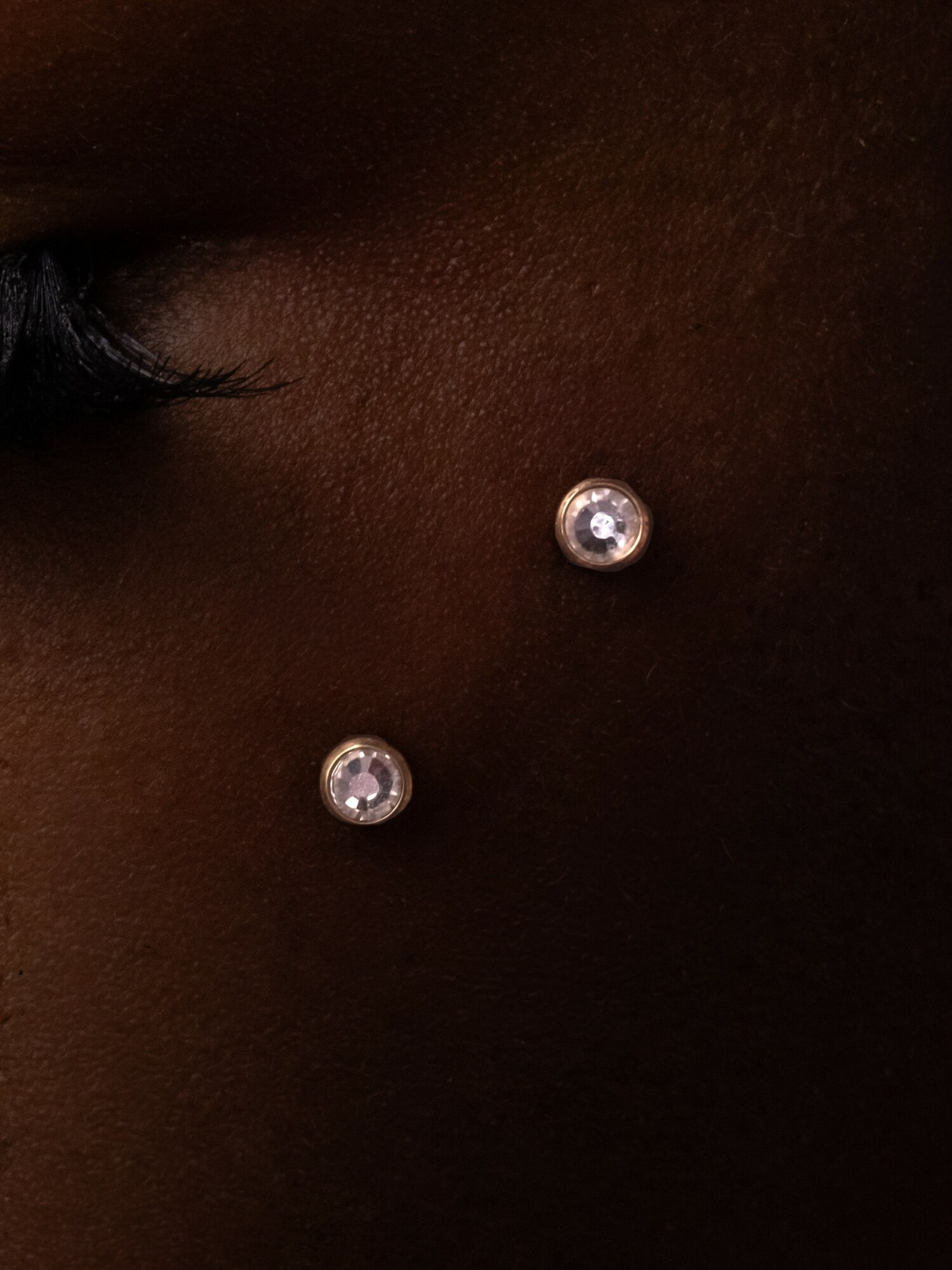 Two small, round, shiny objects on dark skin, possibly jewelry or piercings, positioned vertically.