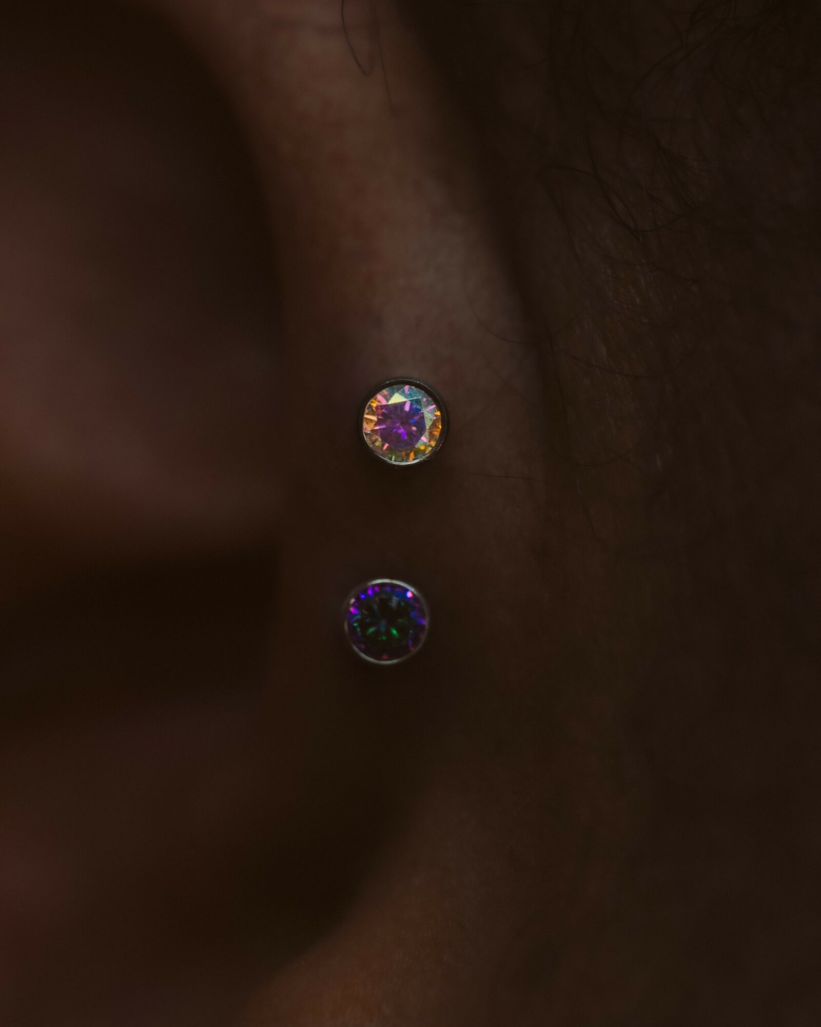 Close-up of a person's ear with a small, round, iridescent earring reflecting light.