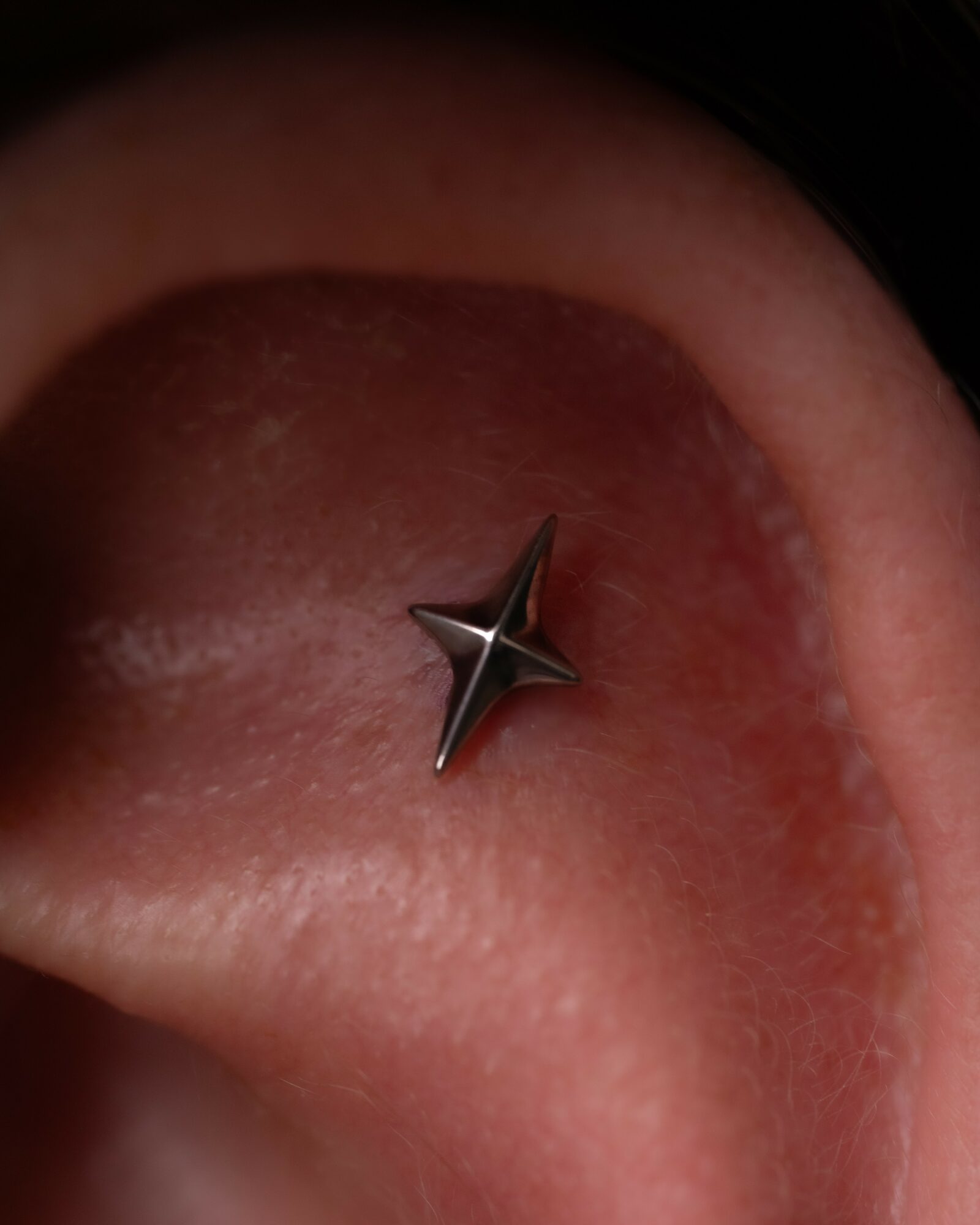 Close-up of a tongue with a metallic star-shaped piercing in the center.